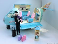 a barbie doll standing next to a toy airplane with luggage and suitcases on the ground