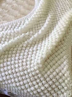 a white crocheted blanket sitting on top of a bed next to a pillow