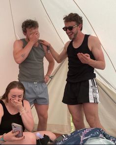 two men standing next to each other in front of a tent while using their cell phones