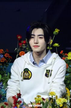 a man sitting in front of flowers wearing a white hoodie with tiger patches on it