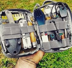 an open tool bag filled with tools on top of a green grass covered field next to a person's hand