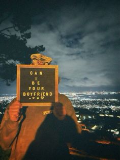 a man holding up a sign that reads can i be your boyfriend? at night