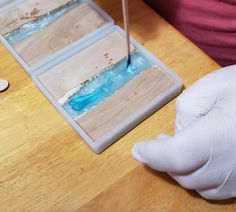 a person in white gloves is working on something with blue liquid and wood planks