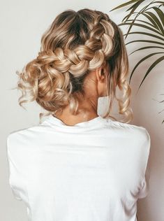 a woman with blonde hair wearing a white shirt and braiding her hair into a bun