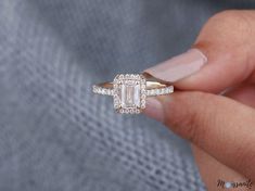 a woman's hand holding a ring with an emerald stone and diamonds on it