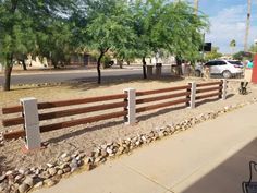 a wooden fence in the middle of a dirt area with rocks and gravel around it