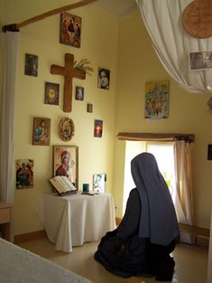 a person sitting in a room with pictures on the wall and a cross above them