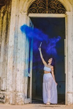 a woman in a white dress is throwing blue powder into the air at an open door