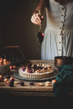 a woman is spooning cherries from a pie on a table with other desserts