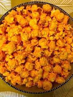 a bowl filled with yellow popcorn sitting on top of a colorful tablecloth covered table