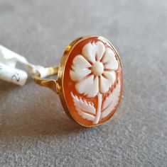 "Shell cameo ring featuring a flower hand carved from orange Carnelian seashell and set in 9 kt gold. Cameo size: 1,7 cm Ring size: on request Contact me for any other request | Customized works also available. Our cameo tecnique respects the ancient cameo tradition consisting in a shell, gemstone, coral, mother of pearl carved with a design in low relief in which the raised design and the background consist of layers of contrasting colours. Every item is really unique because it is carved by ha Yellow Gold Cameo Signet Ring As Gift, Fiance Ring, Ancient Jewels, Cameo Bracelet, Orange Carnelian, Contrasting Colours, Ring Flower, Cameo Jewelry, Cameo Ring