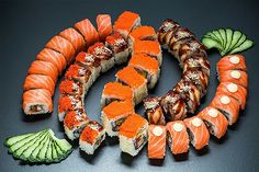 an assortment of sushi and vegetables arranged in a circle on a black table top