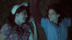 two people sitting in the grass at night with their arms around each other and smiling