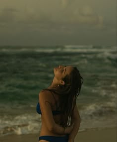 a woman standing on top of a sandy beach next to the ocean with her eyes closed