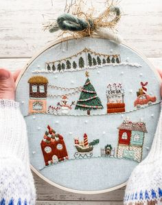 someone holding up a cross stitch christmas ornament in front of a white wooden background