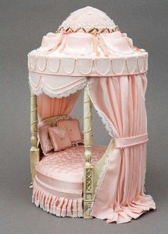 a dollhouse bed with pink sheets and curtains on it's sides, made to look like a canopy