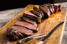 steak sliced up on a cutting board next to a knife and fork with the text marinated venison steaks get the recipe