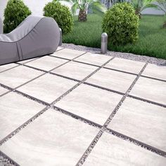 a grey couch sitting on top of a cement floor next to a lush green field