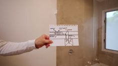 a person holding up a piece of paper in front of a bathroom mirror that has drawings on it