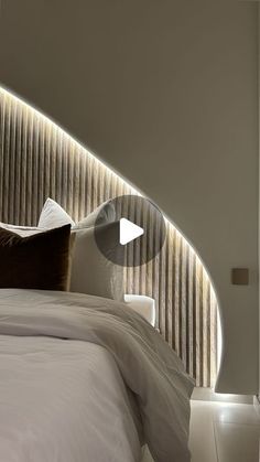 a bed with white sheets and pillows under a curved light fixture on the wall above it