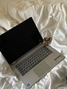 an open laptop computer sitting on top of a white bed covered in sheets and pillows