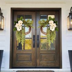 two wreaths on the front door of a house decorated with flowers and greenery