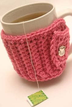 a knitted cup cozys up with a tea in it and is next to a tag