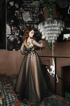 a woman in a black dress standing next to a chandelier with flowers on it