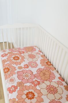 a white crib with a pink and orange flowered sheet on the bedding