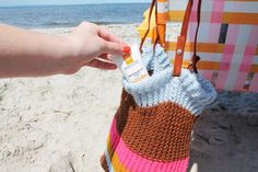 a hand is holding an orange and pink bag on the beach