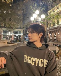 a young man wearing a hoodie standing in front of a park bench at night