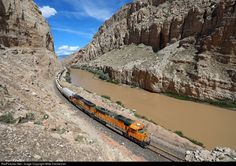 an orange train traveling through a canyon next to a mountain side covered in mud and rocks