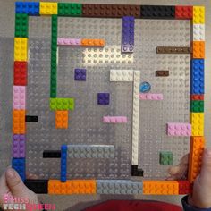 a person holding up a lego board made out of different colored blocks and pieces in the shape of a maze