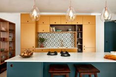 a kitchen with two stools in front of the counter and an island that has three lights hanging over it