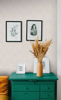 a green dresser with two pictures on the wall and a plant in a vase next to it