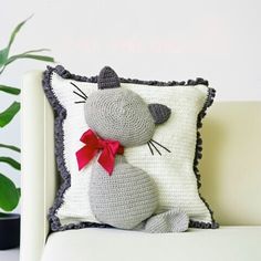 a crocheted cat pillow sitting on top of a white couch next to a potted plant