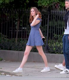 a woman in a blue dress is walking down the street while a man looks on