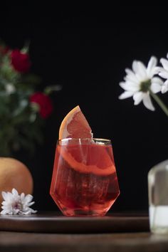 a drink with an orange slice in it on a table next to flowers and other items