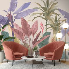 two chairs and a table in front of a wall mural with tropical leaves on it