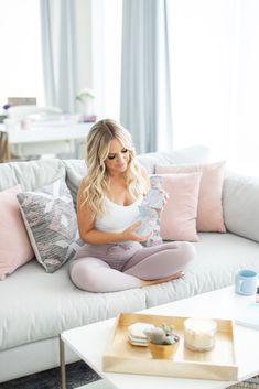 a woman sitting on top of a white couch next to a coffee table and pillows