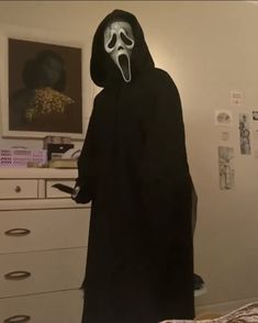 a person wearing a ghost mask and black robe in a room with white drawers, dressers and pictures on the wall