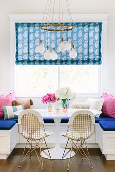 a dining room table with two chairs and a bench in front of a window that has blue roman shades on the windowsill