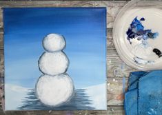 a snowman painting next to a white bowl and blue towel on a wooden table