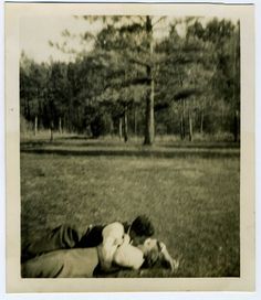 two people laying in the grass with trees in the background and one person holding another