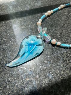 a necklace with a blue flower and beads on it sitting on a marble table next to a glass bead necklace