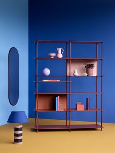 a room with blue walls and a red shelving unit next to a round mirror