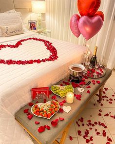 a table topped with lots of food next to a bed covered in red rose petals