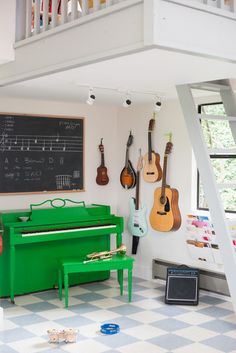 a green piano in the middle of a room with musical instruments on the wall and stairs above it