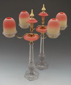 four glass candlesticks with pink and yellow shades on them, one is turned upside down