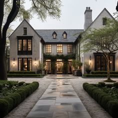 a large white house with lots of windows and plants on the front lawn, surrounded by greenery